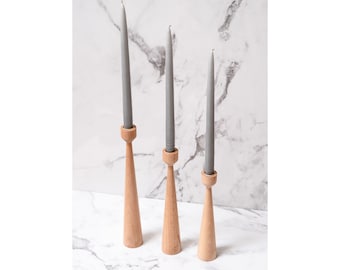 May include: Three wooden candle holders with grey candles. The holders are tapered and have a round top. The candles are all the same size and are about 25 cm tall.