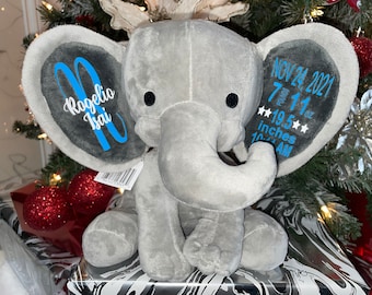 May include: Gray plush elephant baby toy with embroidered details. One ear has the name "Rogelio Isai" in blue lettering. The other ear has the date "NOV 24 2021", time "7:11 AM", weight "7 lb 11 oz", and length "19.5 inches".