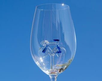 May include: A clear glass wine glass with a blue glass bicycle sculpture inside. The bicycle is made of glass and has a blue frame and wheels.