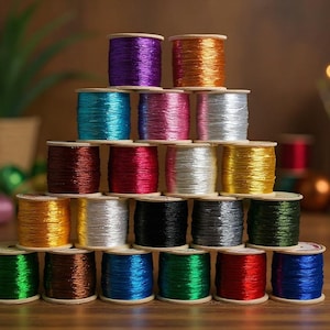 May include: A pyramid arrangement of twenty-one wooden spools wrapped in metallic thread. The collection features a vibrant spectrum of colours including purple, orange, teal, pink, silver, red, magenta, gold, yellow, black, grey, green, and blue.