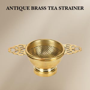 May include: Antique brass tea strainer with a fine mesh and ornate handles. The strainer has a round base and a funnel-shaped top.