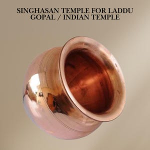 May include: A copper bowl with a rounded bottom and a wide rim. The bowl is shiny and has a slight patina. It is used for holding laddu, a sweet treat often offered in Hindu temples.