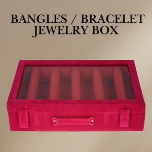 Puede incluir: Una caja de joyería de terciopelo rojo con una tapa transparente y un asa. La caja tiene ocho compartimentos para guardar pulseras o brazaletes. La caja está etiquetada como "Bangles / Bracelet Jewelry Box".