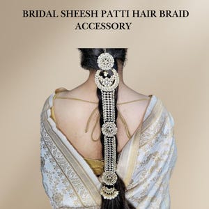 May include: A bridal hair braid accessory with a gold and white design. The accessory features a series of round, decorative pieces with white stones and a dangling pearl.