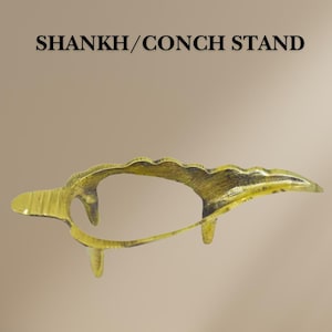 May include: A gold-coloured metal stand shaped like a conch shell, designed to hold a conch shell. The stand has three legs and a curved top.