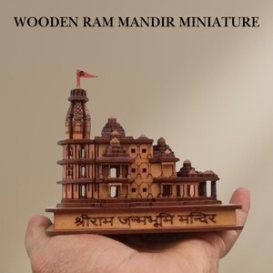 May include: A detailed wooden miniature temple, featuring multiple levels and a flag. The model is a warm brown colour and has text at the base and top. The text at the top reads "WOODEN RAM MANDIR MINIATURE". The base of the model has text in a foreign language.