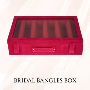 Puede incluir: Una caja rectangular de brazaletes de terciopelo magenta con tapa de cristal transparente. La caja tiene un asa y está dividida en múltiples compartimentos. El texto "BRIDAL BANGLES BOX" está impreso en la parte inferior.