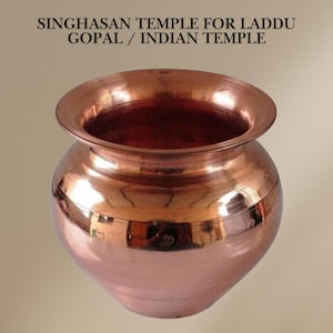 May include: A copper-colored, round pot with a wide, flared rim. The pot has a smooth, reflective surface, and the interior is a darker shade of copper. The text "SINGHASAN TEMPLE FOR LADDU GOPAL / INDIAN TEMPLE" is at the top.