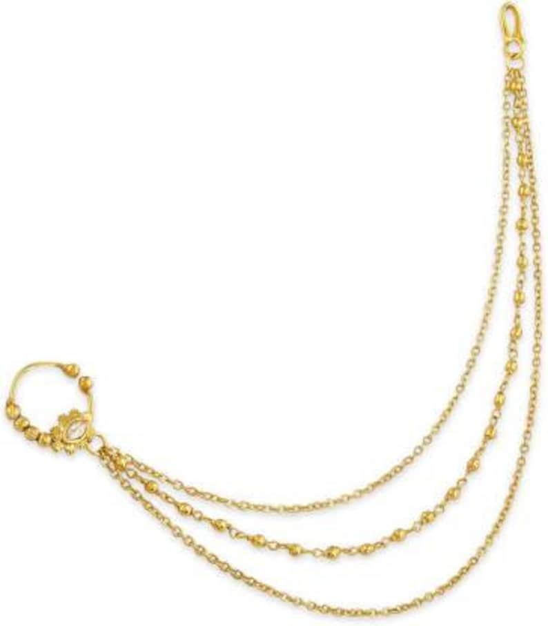 May include: Gold nose ring with a chain that hangs down the side of the face. The chain has three strands of small gold beads.