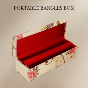 May include: Open, rectangular bangle box with a floral pattern in pink and beige. The interior is lined with red fabric. The box is labeled "PORTABLE BANGLES BOX" in black text.