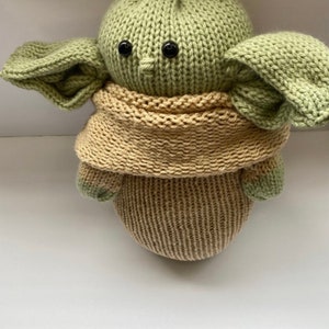 May include: A knitted green and brown plush toy resembling a popular fictional character. The toy has large ears, a small nose, and black button eyes.