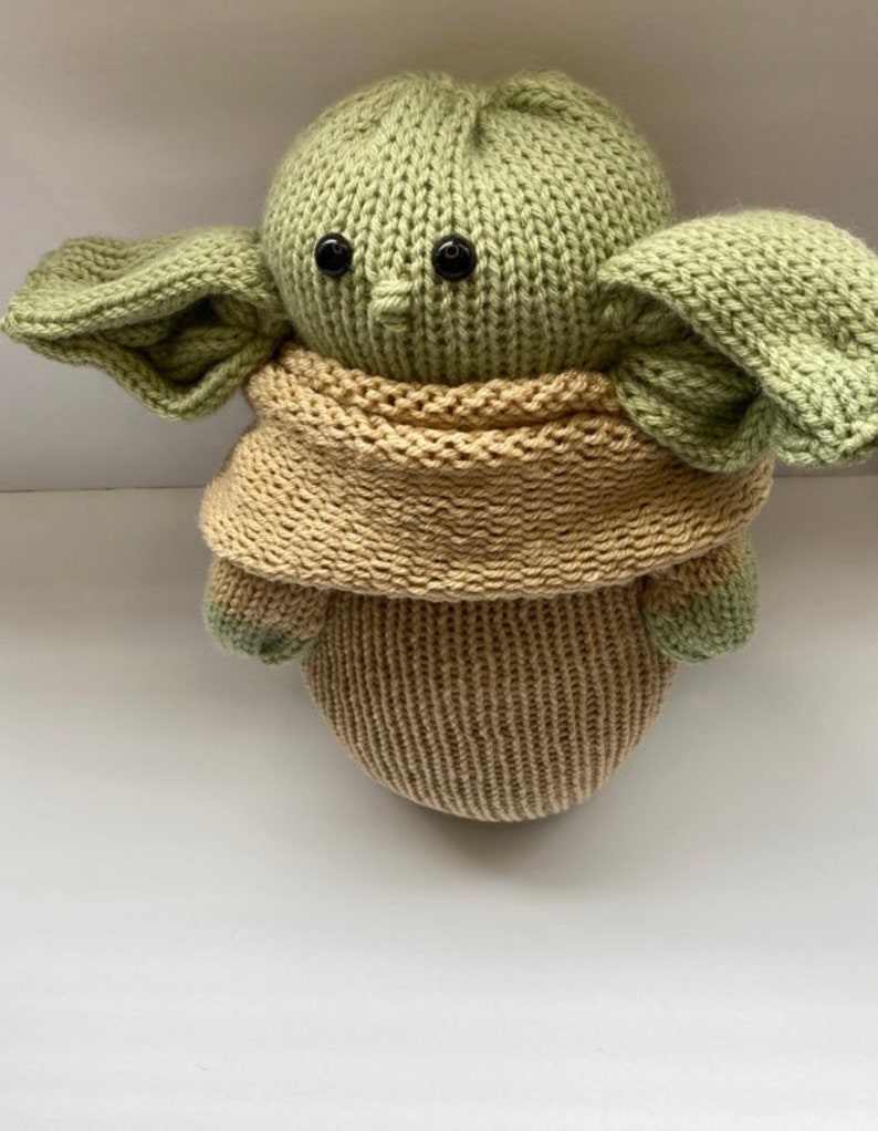 May include: A knitted green and brown plush toy resembling a popular fictional character. The toy has large ears, a small nose, and black button eyes.