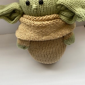 May include: A knitted green and brown plush toy with large ears and black eyes. The toy is wearing a brown knitted scarf.