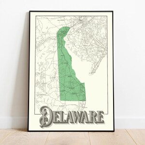 May include: Framed map print of Delaware, featuring a green outline of the state against a cream-colored background. The map includes road networks and geographical details. The word "DELAWARE" is displayed in a 3D-style font at the bottom.