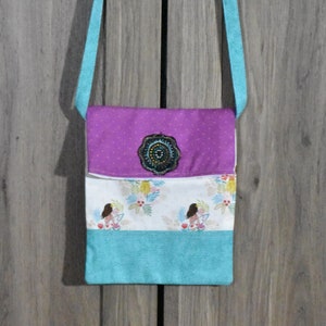 May include: A small purple and turquoise fabric bag with a floral print and a beaded embellishment. The bag has a long turquoise strap.