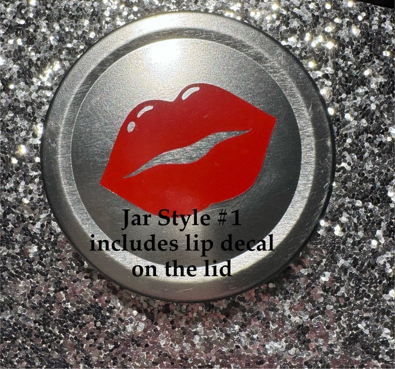 May include: A silver jar lid with a red lip decal. The text "Jar Style #1 includes lip decal on the lid" is printed below the lip graphic. The lid is set against a sparkly, silver background.