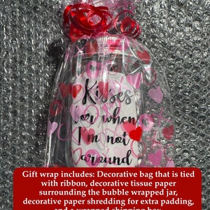 May include: A clear glass jar wrapped in cellophane with pink and red hearts and a red ribbon. The jar has the words "Kisses for when I'm not around" written on it. The jar is wrapped in bubble wrap.