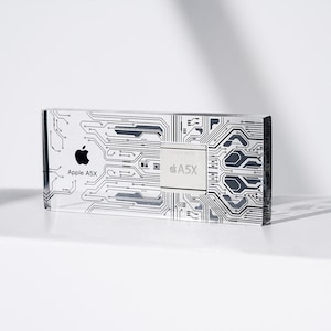 Puede incluir: Un pisapapeles de vidrio transparente con un diseño de placa de circuito negro y blanco. El pisapapeles presenta el logotipo de Apple y el texto "Apple A5X".