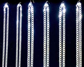 Puede incluir: Cinco cadenas de plata de diferentes longitudes colgando de ganchos sobre un fondo negro. Las cadenas son todas del mismo estilo, con un diseño de eslabón de curb.