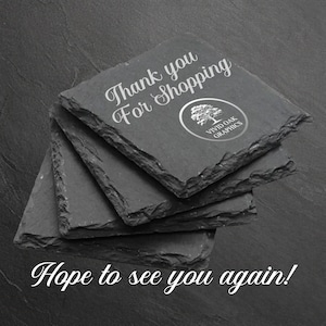 Puede incluir: Un conjunto de cuatro posavasos de pizarra negra con el texto "Gracias por comprar" y un logotipo que dice "Vivid Oak Graphics". El texto "&iexcl;Esperamos verte de nuevo!" est&aacute; escrito debajo de los posavasos.