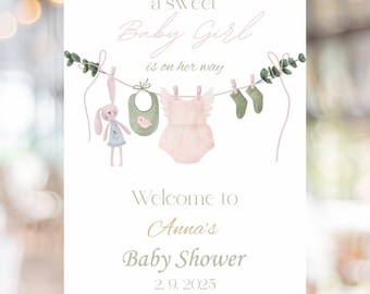 Op de afbeelding: Een babyborrelbord op een gouden ezel. Het bord leest "a sweet Baby Girl is on her way". Het bevat illustraties van babykleding en een konijn. Het bord verwelkomt gasten op Anna's Baby Shower op 2.9.2025.