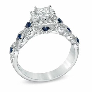 May include: A silver engagement ring with a square-cut center stone surrounded by smaller diamonds. The band is adorned with smaller diamonds and blue sapphires.