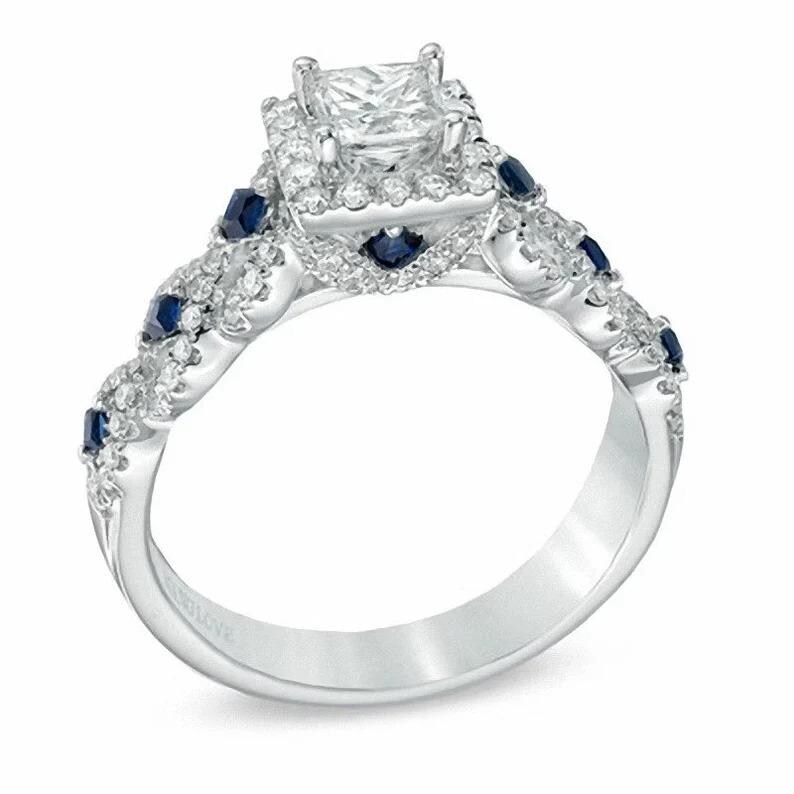 May include: A silver engagement ring with a square-cut center stone surrounded by smaller diamonds. The band is adorned with smaller diamonds and blue sapphires.