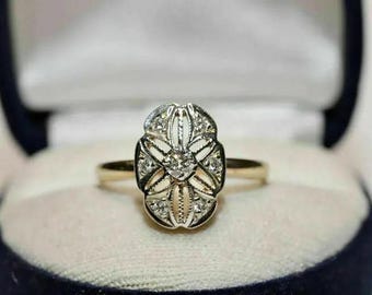 May include: A vintage gold ring with an oval, filigree-style setting. The setting is adorned with small diamonds and a larger central stone. The ring is presented in a blue jewelry box with a white interior.