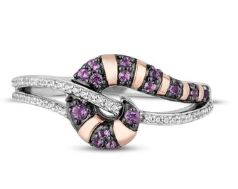 May include: A silver ring with a rose gold and black swirl design. The swirl is set with purple gemstones and the band is accented with smaller white gemstones.