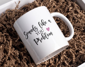 May include: White ceramic mug with the text "Sounds like a YOU Problem" in black script, with a small pink heart. The mug is inside a white box filled with brown crinkle paper.
