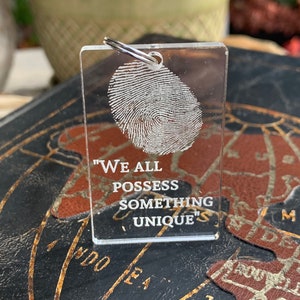 May include: A clear acrylic keychain with a fingerprint design and the text "We all possess something unique".