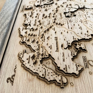 May include: A wooden map of the fictional world of Tamriel, featuring the regions of Skyrim, High Rock, Hammerfell, and Cyrodil. The map is laser-cut and engraved with detailed borders and text.