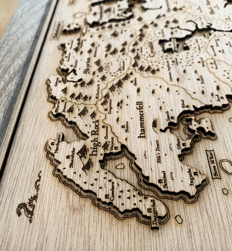 May include: A wooden map of the fictional world of Tamriel, featuring the regions of Skyrim, High Rock, Hammerfell, and Cyrodil. The map is laser-cut and engraved with detailed borders and text.