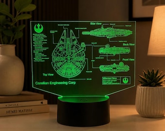 Op de afbeelding: Een groene LED-acryllamp met een technisch blauwdrukontwerp van de Millennium Falcon. Het display toont bovenaanzichten, zijaanzichten, achteraanzichten en vooraanzichten met labels zoals Corellian Engineering Corp en diverse scheepsonderdelen op een zwarte voet.