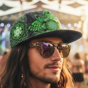 May include: A person wearing a patterned baseball cap with green and black designs, and sunglasses with a decorative frame. The sunglasses reflect a crowd. The person has long, wavy brown hair with colourful beads.