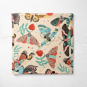 May include: A cream-colored fabric with a repeating pattern of colorful butterflies and red flowers. The butterflies are in various shades of blue, pink, orange, and black.