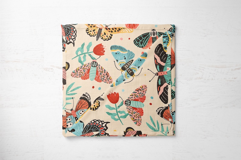 May include: A cream-colored fabric with a repeating pattern of colorful butterflies and red flowers. The butterflies are in various shades of blue, pink, orange, and black.