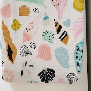 May include: A white fabric with a repeating pattern of colorful seashells. The shells are in various shapes and sizes, including spiral, clam, and oyster.