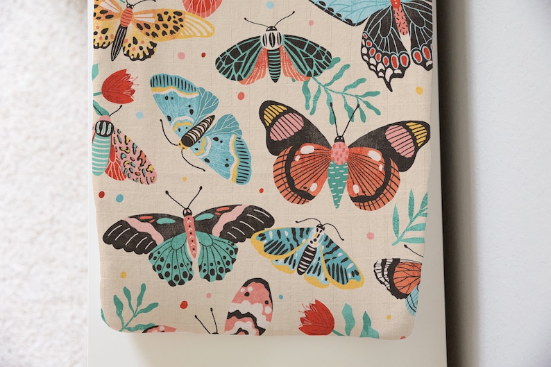 May include: A beige fabric with a repeating pattern of colorful butterflies. The butterflies are in various shades of blue, pink, red, yellow, and green. The fabric has a subtle texture.