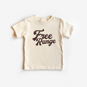May include: A cream colored short-sleeved t-shirt with a brown graphic that says "Free Range" in a retro font.
