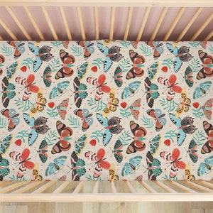 May include: A fitted crib sheet with a colorful butterfly pattern on a beige background. The butterflies are in shades of blue, red, orange, and yellow.