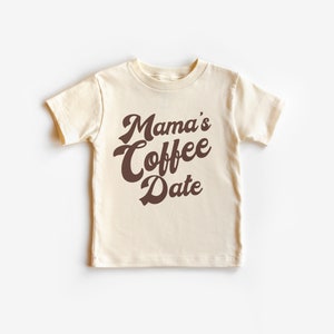 May include: A cream colored t-shirt with brown text that reads "Mama's Coffee Date" in a retro font.