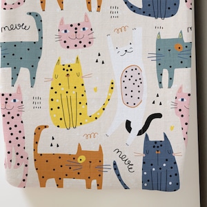 May include: A white fabric with a repeating pattern of colorful cats with black polka dots. The text "meows" is written on the fabric.