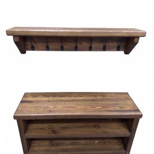Puede incluir: Un perchero de pared de madera marr&oacute;n oscuro con siete ganchos de metal negro y un banco de madera rectangular a juego con dos estantes de almacenamiento abiertos. Ambas piezas muestran una textura de veta de madera visible y un acabado te&ntilde;ido.