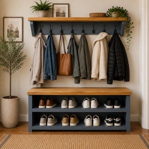 Puede incluir: Un mueble de entrada montado en la pared con un marco de madera azul oscuro, una repisa superior de madera natural y un banco a juego con dos niveles de almacenamiento abiertos. Incluye ocho ganchos de metal negro con varios abrigos y un bolso.