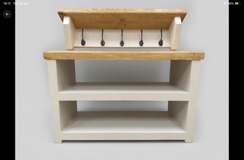 Puede incluir: Un banco de entrada de madera con una superficie de madera natural y una base de color crema con dos estantes abiertos. En la parte superior, un perchero de pared a juego cuenta con cinco ganchos de metal negro y una repisa de madera.