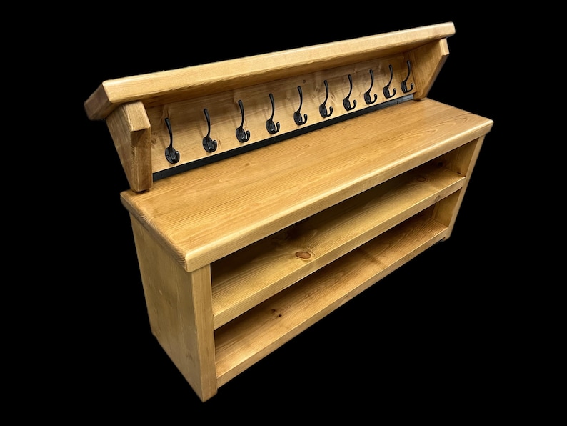 Puede incluir: Un banco de entrada de madera marr&oacute;n claro que cuenta con un estante superior con diez ganchos de metal negro y dos estantes de almacenamiento abiertos en la parte inferior. La unidad es de madera natural con veta visible y superficie lisa.
