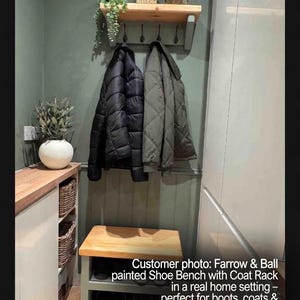 Puede incluir: Un banco zapatero de madera con estante inferior y un perchero de pared a juego con cuatro ganchos negros. El mueble est&aacute; pintado en un tono verde apagado con superficies de madera natural, sosteniendo dos chaquetas y varios pares de zapatos.