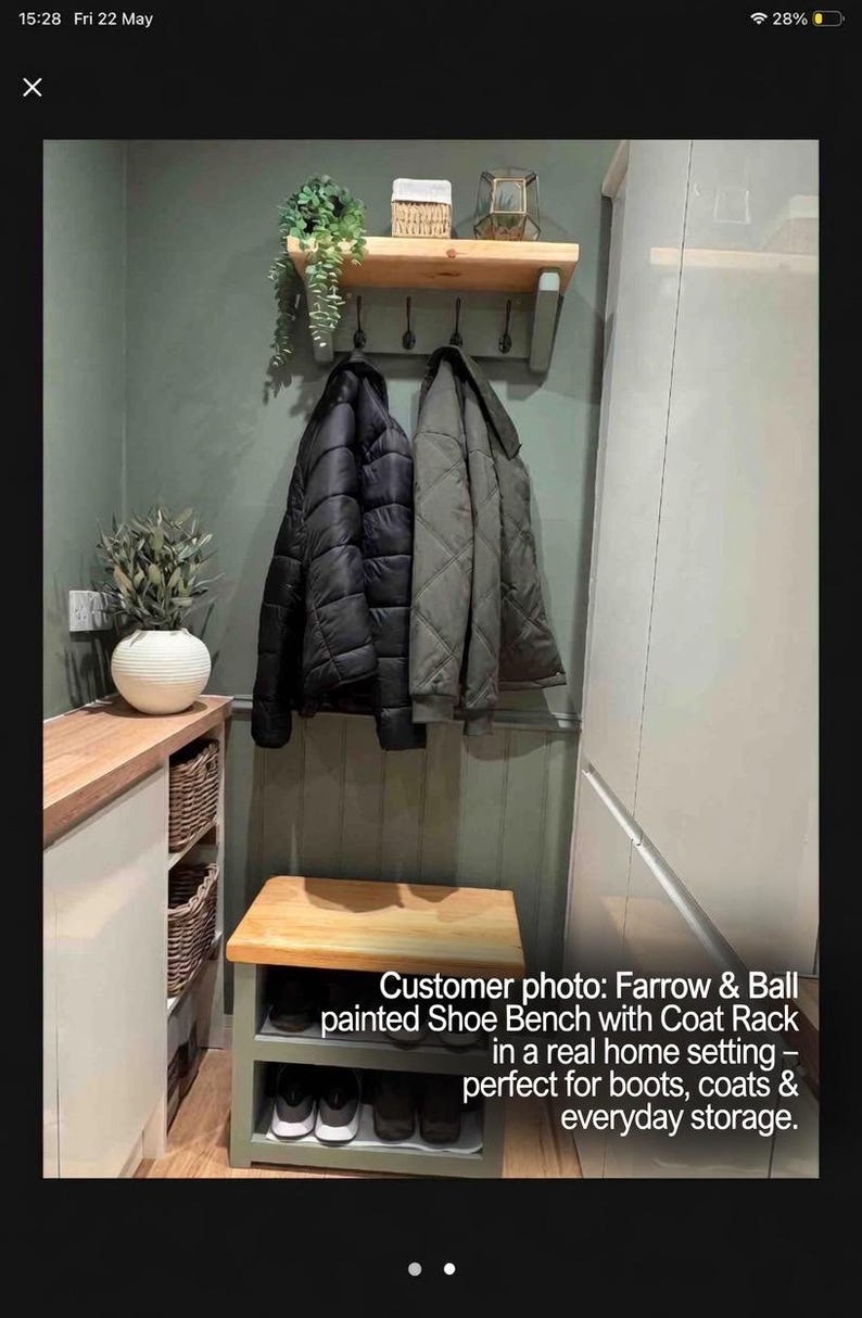 Puede incluir: Un banco zapatero de madera con estante inferior y un perchero de pared a juego con cuatro ganchos negros. El mueble est&aacute; pintado en un tono verde apagado con superficies de madera natural, sosteniendo dos chaquetas y varios pares de zapatos.