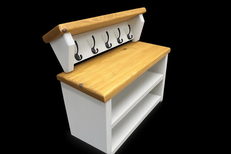 Puede incluir: Un banco de entrada de madera blanca con una superficie superior en tono madera natural, dos estantes de almacenamiento abiertos y un panel trasero con cinco ganchos de metal negro. La unidad tiene una construcci&oacute;n robusta y contrastada.